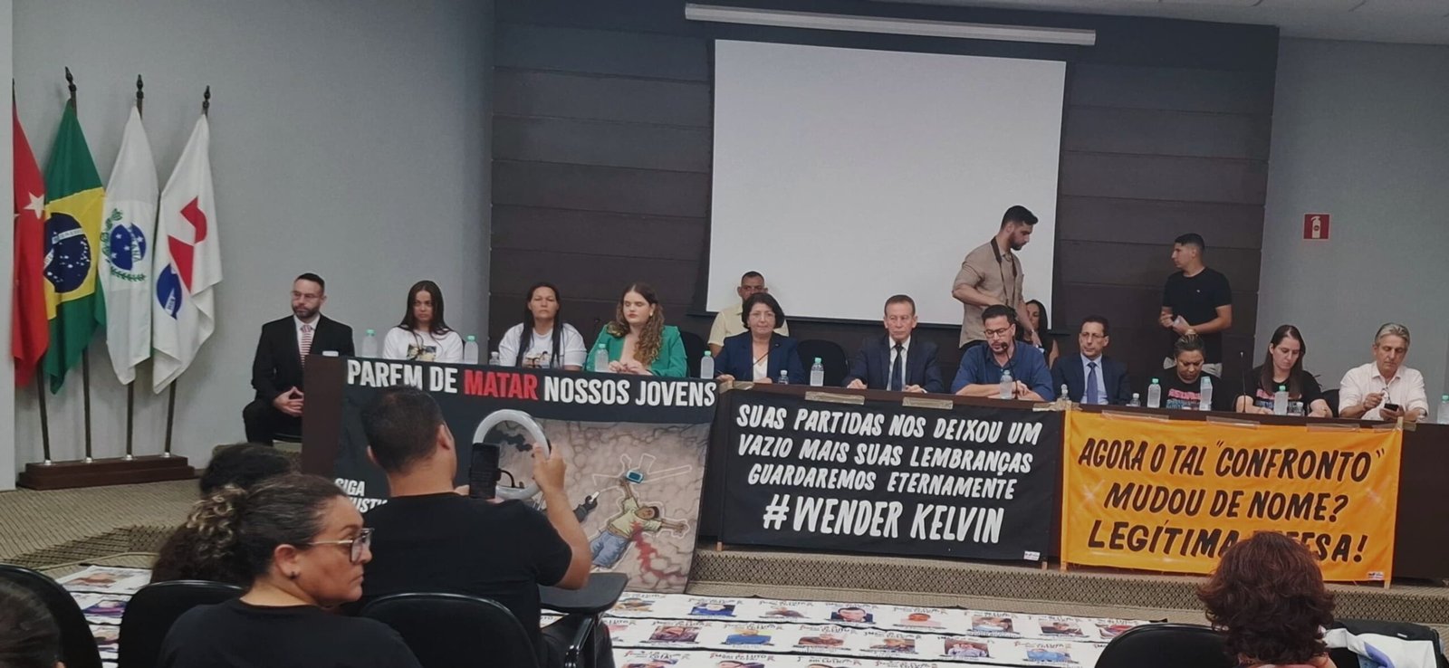 Mesa de audiência pública da Assembleia Legislativa do Paraná em Londrina sobre violência policial, com faixas de protesto e participação de autoridades e familiares