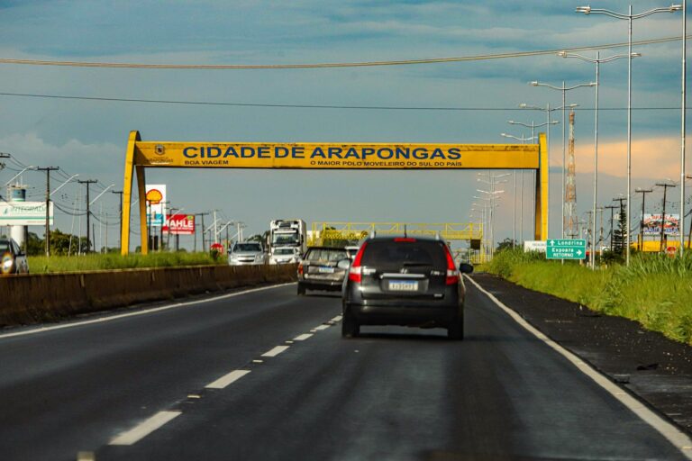 Placa amarela na rodovia indicando a entrada da cidade de Arapongas, no Norte do Paraná, com o slogan “O maior polo moveleiro do Sul do país”.