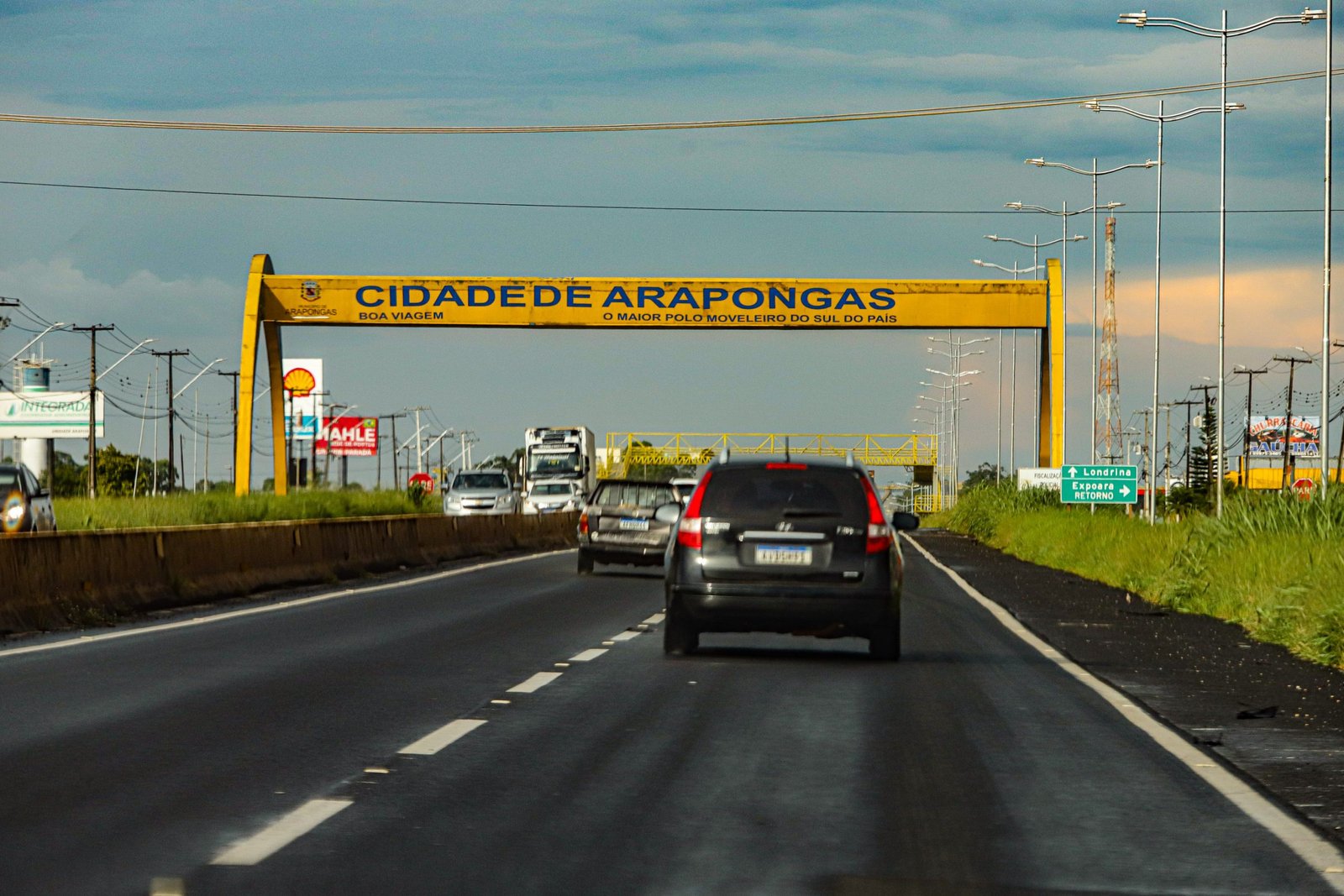 Placa amarela na rodovia indicando a entrada da cidade de Arapongas, no Norte do Paraná, com o slogan “O maior polo moveleiro do Sul do país”.