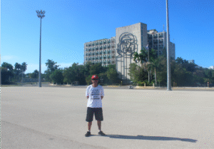 Tiago Prado na Praça da Revolução em Havana, Cuba, com o prédio do Ministério do Interior e a imagem icônica de Che Guevara ao fundo.
