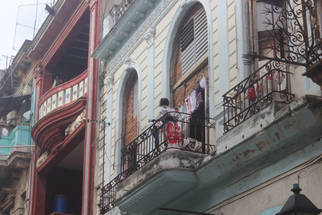 Mulher na sacada de um prédio antigo com tijolos aparentes estendendo roupas.