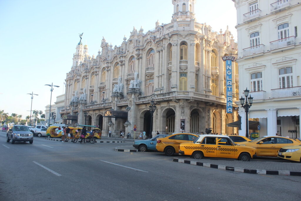 Fachada ornamentada do Hotel Inglaterra com táxis amarelos estacionados em frente