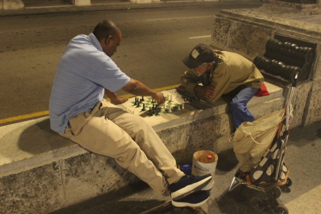 Dois homens jogando xadrez sentados em um banco de pedra à noite